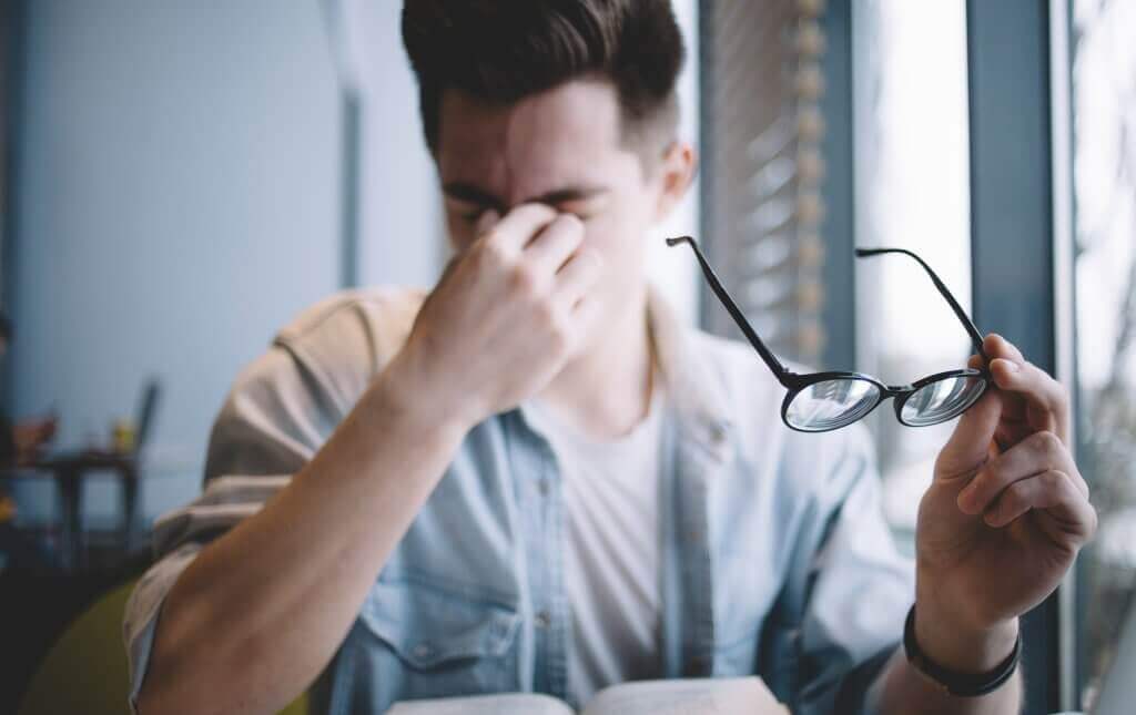 mann der im Hintergrund verschwommen ist, reibt sich die Augen und hält seine Lesebrille in einer Hand