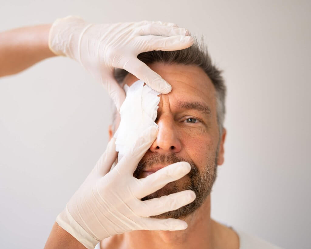 Mann nach Augenlaser OP mit Schutzbinde vor dem Auge