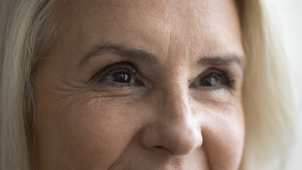 Nahaufnahme von Augen und Gesichtsfalten einer älteren Frau mit blonden Haaren.