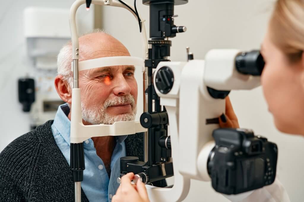 Älterer Mann bei Augenuntersuchung mit Spaltlampe im Optikerzentrum.