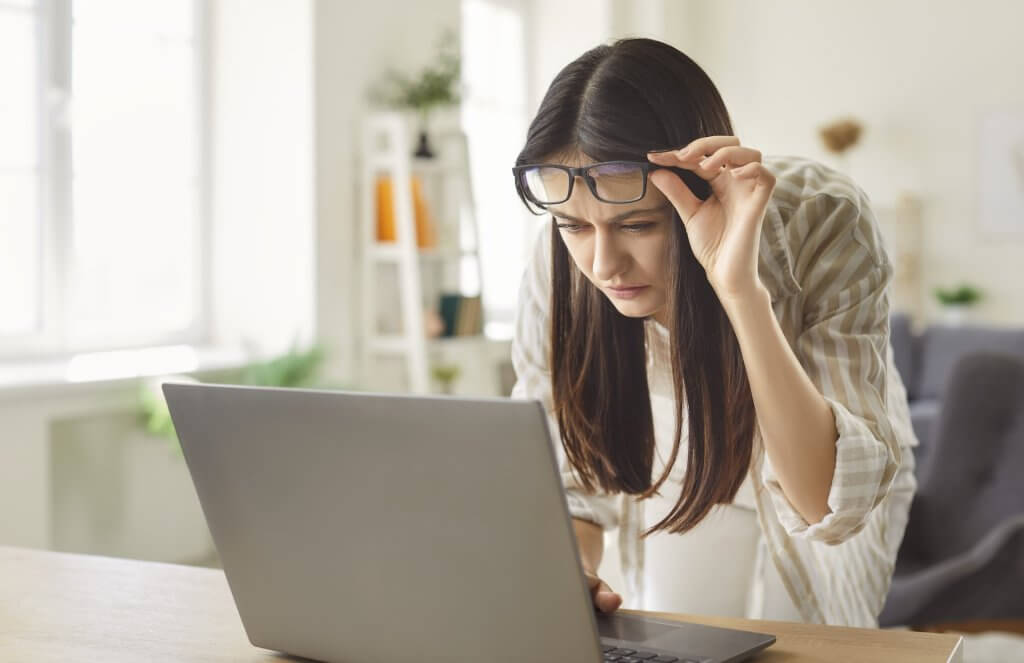 Frau sieht verschwommen auf ihrem Laptop aufgrund einer Hornhautverkrümmung.